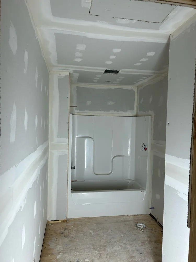 Bathroom around a tub and shower unit with drywall taped and mudded on the walls and ceiling.
