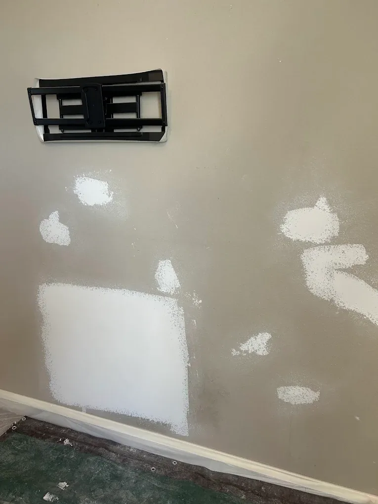 Several patched areas on a painted wall after a TV mount and anchors were removed, prepped for texture and paint matching.